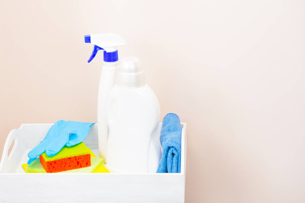 Limpeza da casa usando produtos de limpeza. O conceito de limpeza e conforto. Em um fundo rosa claro, uma bandeja branca, detergente, panos. Feche, vista lateral. Há um lugar para a assinatura
 - Foto, Imagem