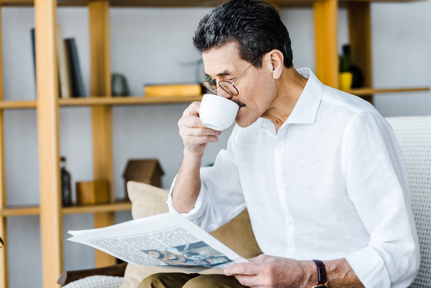 gepensioneerde m/v in glazen drinken koffie en het lezen van de krant thuis - Foto, afbeelding