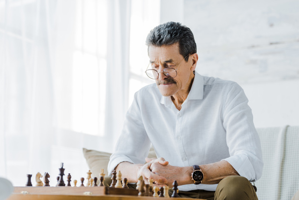 senior man with mustache looking at chess board at home - Foto, immagini