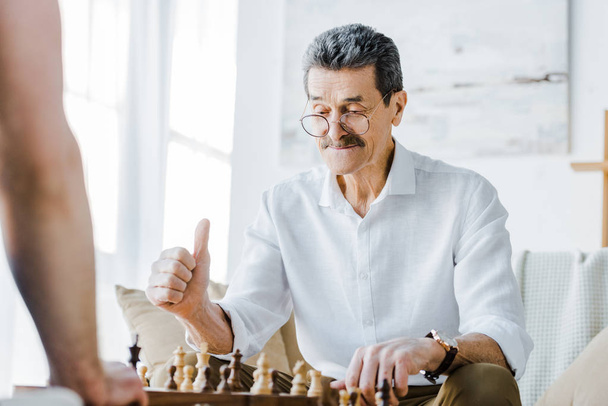 foyer sélectif de l'homme âgé avec moustache montrant pouce vers le haut tout en jouant aux échecs avec un ami à la maison
 - Photo, image