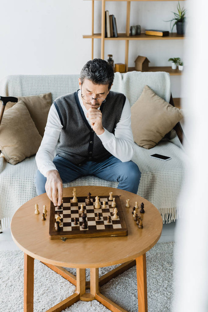 promyšlené bývalý muž v brýlích, při pohledu na šachovnici doma - Fotografie, Obrázek