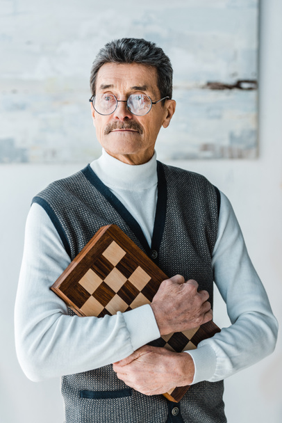 pensive senior man holding chess board at home - Foto, imagen
