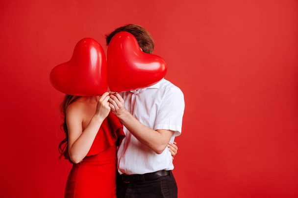 Portrait of attractive young couple posing on red background and holding balloons heart. - Photo, image