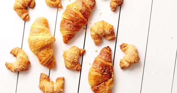 From above shot of set of yummy fresh croissants of assorted sizes lying on surface of white timber tabletop - Footage, Video