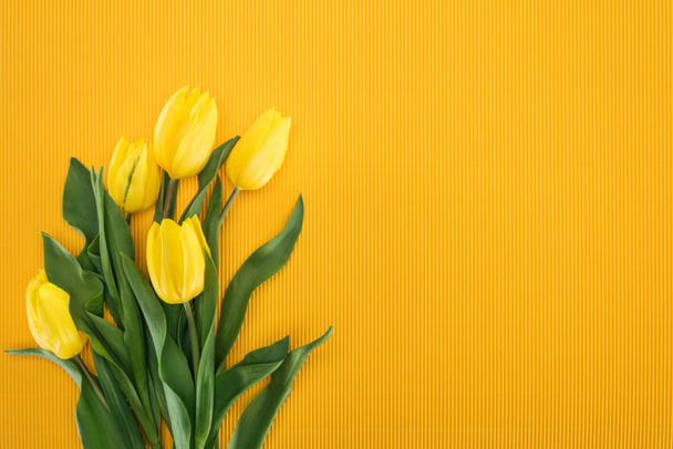 bovenaanzicht van boeket met gele tulpen op een oranje achtergrond - Foto, afbeelding