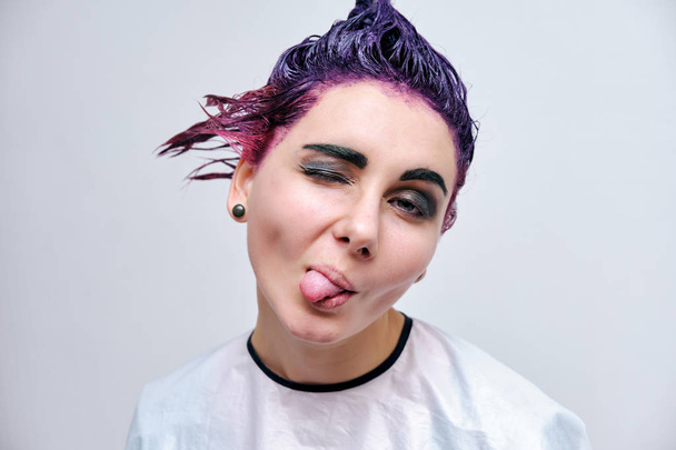 Beautiful girl with violet hair on white background master in make-up. Visible hand of the master and his makeup. The girl is in the middle of the frame and sits on a chair. - Valokuva, kuva