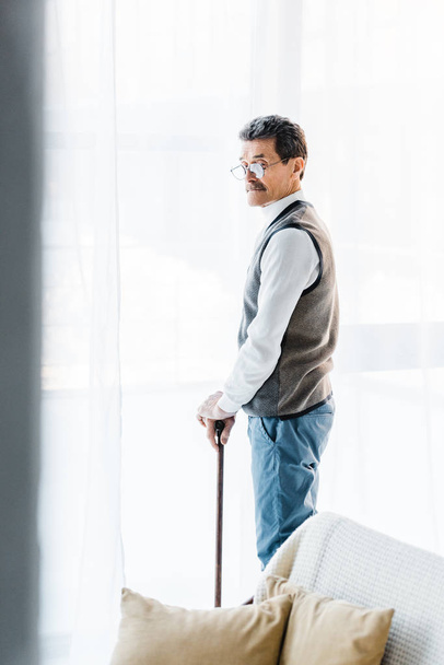 selectieve aandacht van gepensioneerde man die met wandelstok thuis - Foto, afbeelding