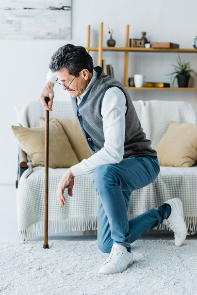 συνταξιούχος άνθρωπος γυαλιά κρατώντας το βάδισμα από ζαχαροκάλαμο προσπαθώντας να στέκεται επάνω στο σπίτι - Φωτογραφία, εικόνα
