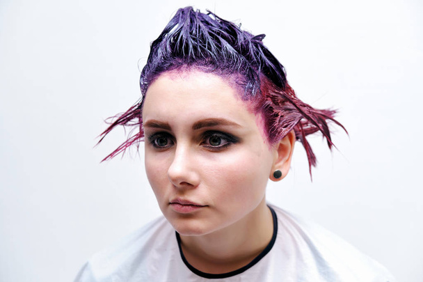 Beautiful girl with violet hair on white background master in make-up. Visible hand of the master and his makeup. The girl is in the middle of the frame and sits on a chair. - Foto, Bild