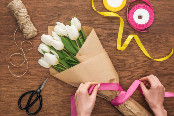 cropped view of on florist making bouquet of spring tulip flowers with ribbon on wooden background - Photo, Image