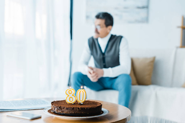 enfoque selectivo de pastel de cumpleaños con velas encendidas con hombre mayor solitario sentado en el fondo
 - Foto, Imagen