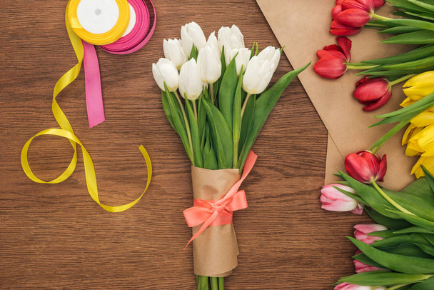 top view of spring bouquet, tulips, ribbons and craft paper on wooden background  - 写真・画像