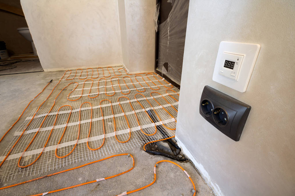 Εγκατασταθεί στο τσιμεντένιο πάτωμα σε μικρά νέα ημιτελές δωμάτιο με το κόκκινο ηλεκτρικών καλωδίων σύρμα σύστημα θέρμανσης σοβατισμένοι τοίχοι. Ανακαίνισης και κατασκευής, σύγχρονη τεχνολογία, άνετο ζεστό σπίτι έννοια. - Φωτογραφία, εικόνα