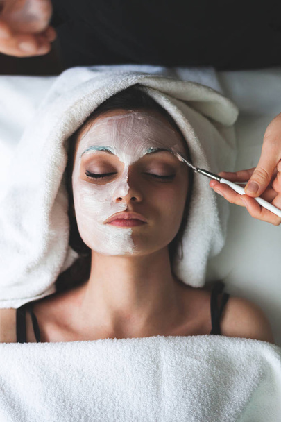 Cosmético aplicando mascarilla de belleza facial para mujer joven y hermosa en el salón de spa
 - Foto, Imagen