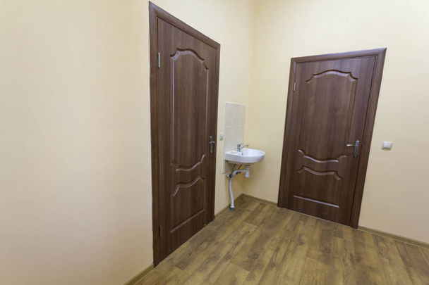 Ahşap zemin, kahverengi kapı ve lavabo ile hafif boş koridor hall. Okul, ofis ya da klinik iç. - Fotoğraf, Görsel