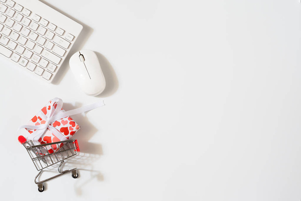 Overhead shot of wireless keyboard and mouse, gifts box with shopping cart. Flat lay  office working space for Valentines' day and women's day shopping online concept. Minimal style top view with copy space. - Photo, Image