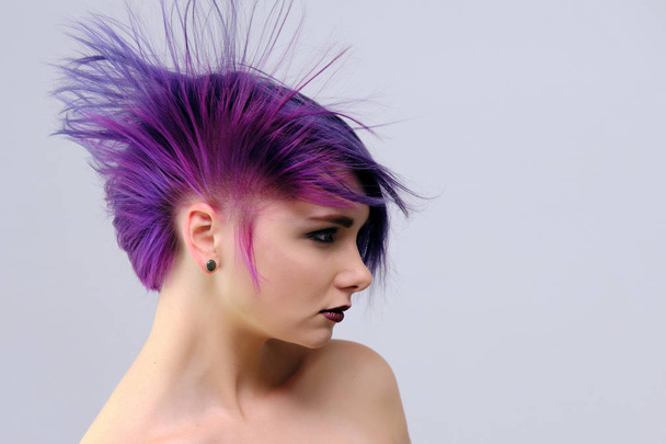 A beautiful, sexy girl with purple hair and a short haircut sits in the middle of the photo with a white background and grimaces. She's naked and visible shoulders. - Foto, Imagem