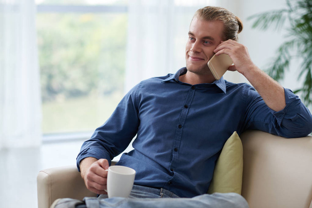 Retrato de un joven guapo sonriente bebiendo café y hablando por teléfono
 - Foto, Imagen
