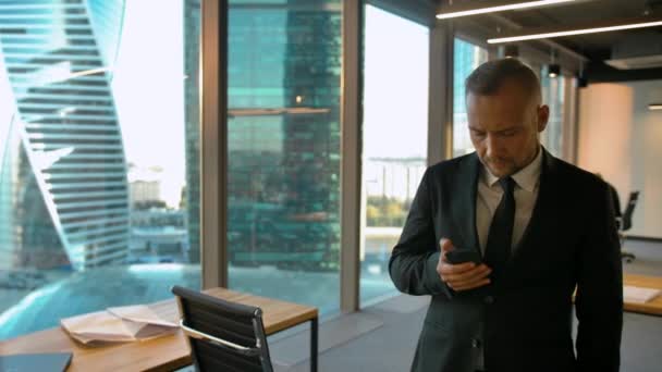 Attrtactive entrepreneur in formal suit standing near window and writing sms - Séquence, vidéo