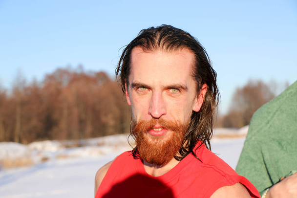 Молодой симпатичный и привлекательный мужчина с мускулистым телом, с рыжей бородой и длинными волосами, мокрый после принятия ледяной ванны. красивые привлекательные мужчины, принимающие душ рядом с бассейном. капли воды падают на его туловище. Солнечный зимний день на Украине
,  - Фото, изображение