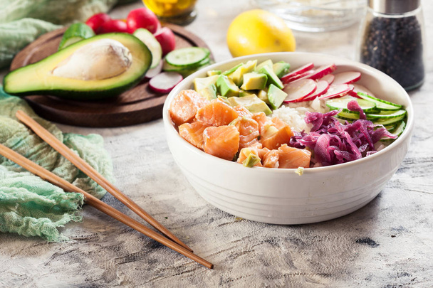 Poke bowl, traditional Hawaiian raw fish salad with rice, avocado, cucumber and radish on bright background - Fotó, kép