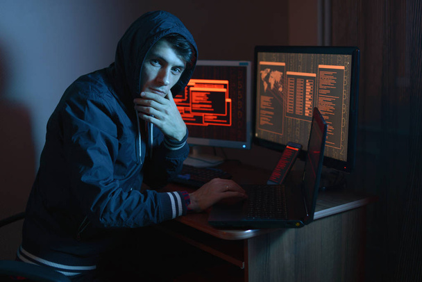 Male in the hood looking in the camera. Hacker attacks and online fraud in the dark on the screen background in neon light. The concept of cyber security - Zdjęcie, obraz