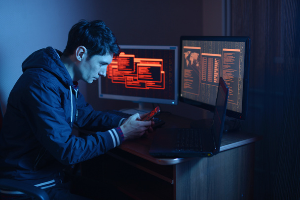 Homem hacker segurando o telefone em suas mãos tentando hackear a nuvem do dispositivo móvel e roubar dados no escuro sob luz de néon. O conceito de cibersegurança
 - Foto, Imagem