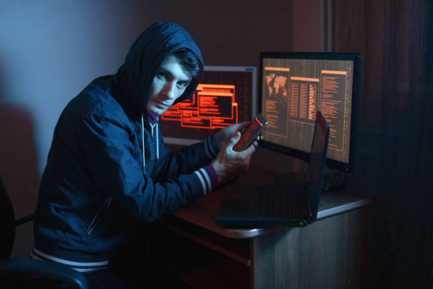 Hacker in the hood holding the phone in his hands trying to hack the mobile device cloud and steal data in the dark under neon light. The concept of cyber security - Photo, Image