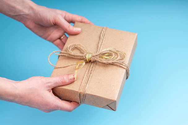 Hands holding gift box Packed in Kraft paper on blue background. Concept holiday card for Valentine's day and women's day - Φωτογραφία, εικόνα