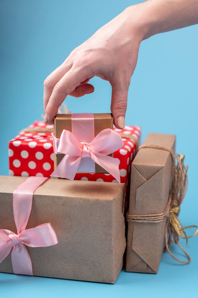 Manos de mujer sosteniendo cajas de regalo Embaladas en papel Kraft con cinta rosa sobre fondo azul. Concepto tarjeta de vacaciones para el día de San Valentín y el día de la mujer
 - Foto, Imagen