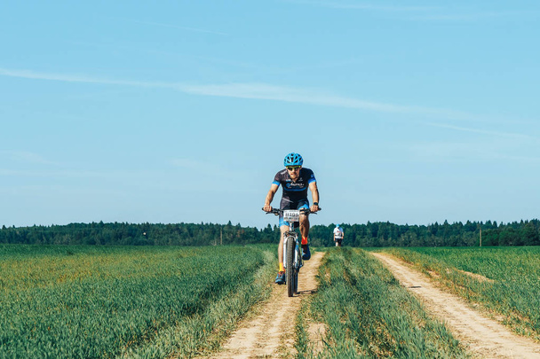 May 26-27, 2018 - Naliboki, Belarus: All-Belarusian amateur marathon Naliboki, man rides bike on rural road in field during race - Foto, Imagen