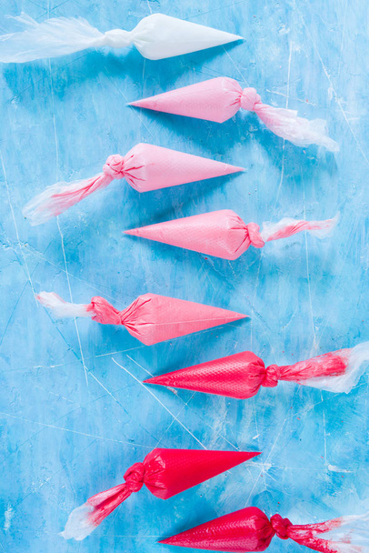 fila de bolsas de plástico con crema rosa en la superficie de hormigón azul
 - Foto, imagen