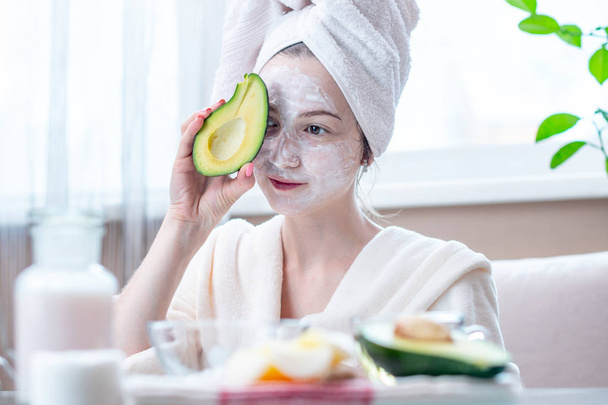 Mulher jovem feliz bonita com máscara de abacate natural cosmético em seu rosto. Conceito cuidados com a pele e tratamentos de Spa em casa
 - Foto, Imagem