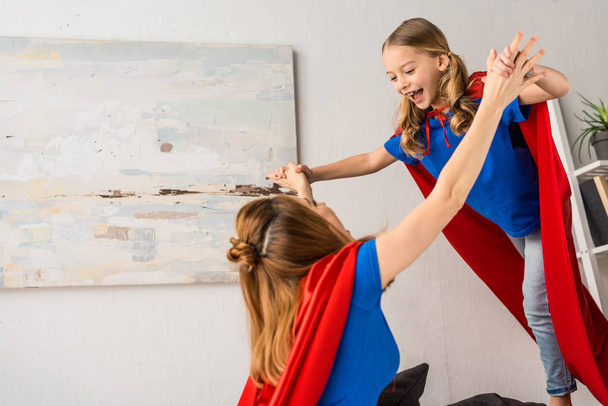 smiling daughter and mother in red cloaks playing at home - Foto, imagen