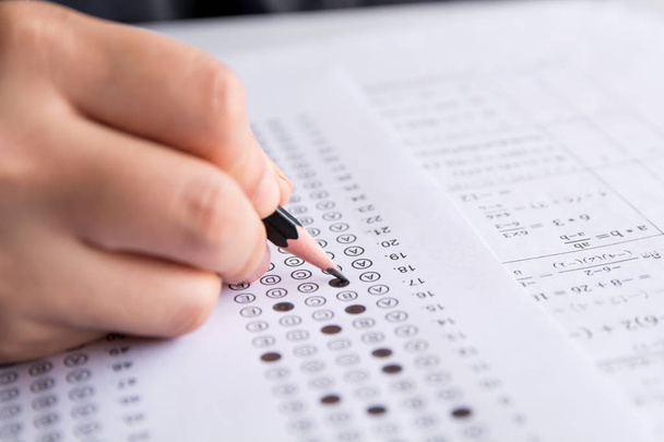 Studenci trzymają ołówek pisząc wybrany wybór na arkuszach odpowiedzi i arkuszach pytań z matematyki. studenci testujący egzamin. egzamin szkolny  - Zdjęcie, obraz