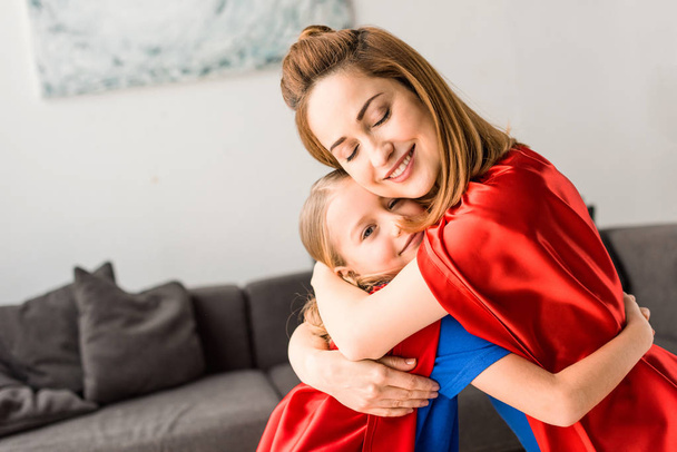 Mignon enfant et mère en manteaux rouges étreignant et souriant à la maison
  - Photo, image