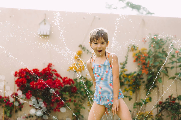 funny little girl running though garden sprinkler  - Fotografie, Obrázek