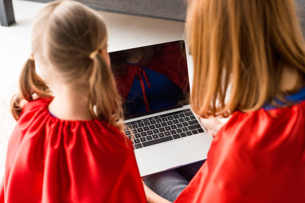 Takaisin näkymä äiti ja tytär punaisissa kaavut katsomalla kannettavan tietokoneen näytön
 - Valokuva, kuva