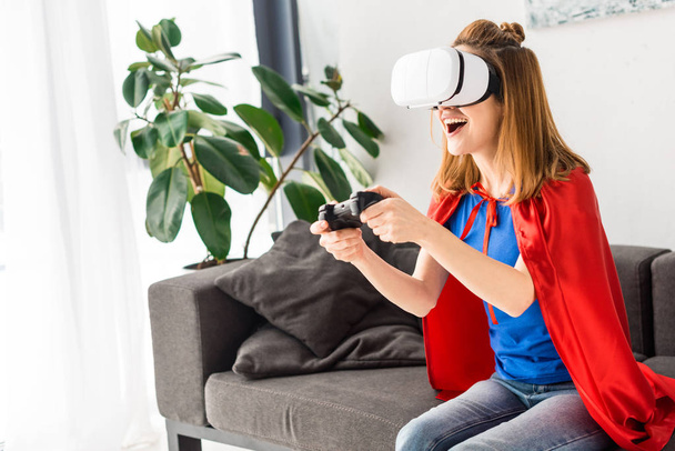 Mère souriante en manteau rouge et casque de réalité virtuelle jouant au jeu vidéo
 - Photo, image