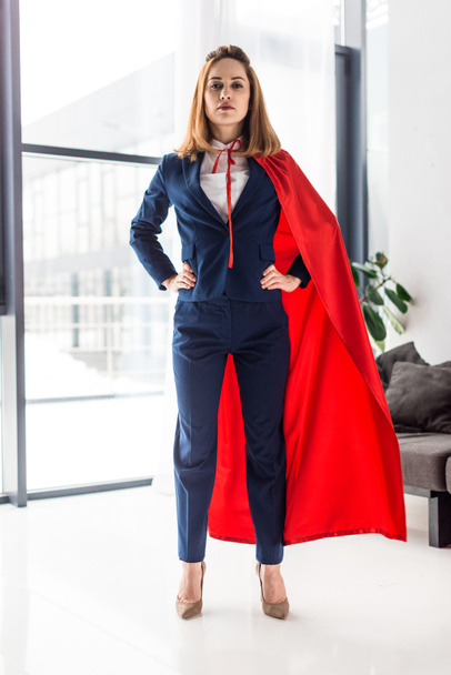 Confident businesswoman in blue suit and red cape looking at camera - Фото, зображення