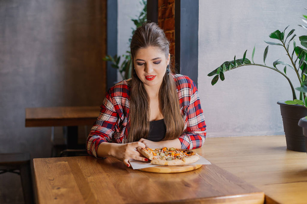 Bir kafede cam kenarında oturan ve pizza tutan güzel ve seksi kız. - Fotoğraf, Görsel
