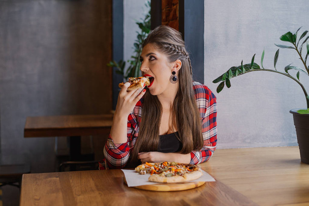 Kaunis ja seksikäs tyttö istuu ikkunan vieressä kahvilassa ja syö pizzaa
. - Valokuva, kuva