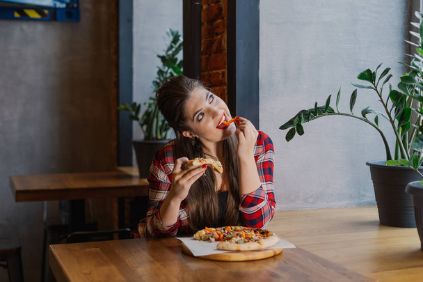 Красивая и сексуальная девушка сидит у окна в кафе и ест пиццу
 - Фото, изображение