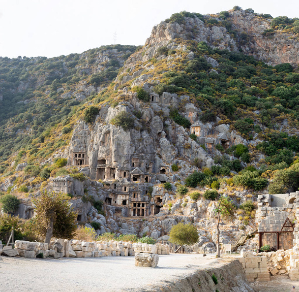 Ancient lycian necropolis with tombs carved in rocks. Tourists walking near Lycian tombs in Mira. - Photo, Image