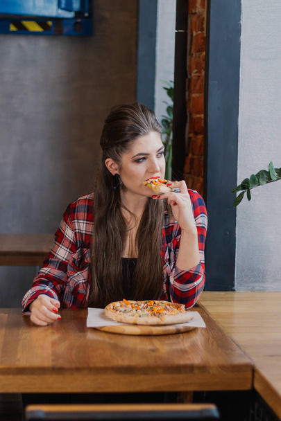 Bir kafede bir pizza ile bir masada oturan güzel ve seksi kız. - Fotoğraf, Görsel