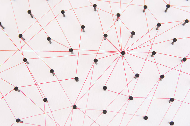 Verknüpfung von Einheiten, sozialen Medien, Kommunikationsnetzen, die Verbindung zwischen den beiden Netzwerken. Netzwerksimulation auf weißem Papier, verknüpft durch schwarzen Nagel und roten Faden - Foto, Bild