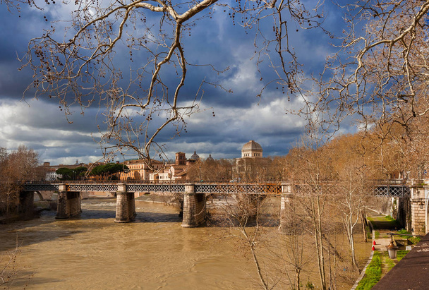 Stormy clouds in winter Rome along River Tiber, view through bare branch trees - Foto, Imagem