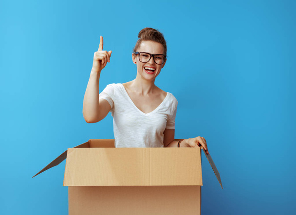 happy young woman in white t-shirt in a cardboard box got idea isolated on blue background - Φωτογραφία, εικόνα