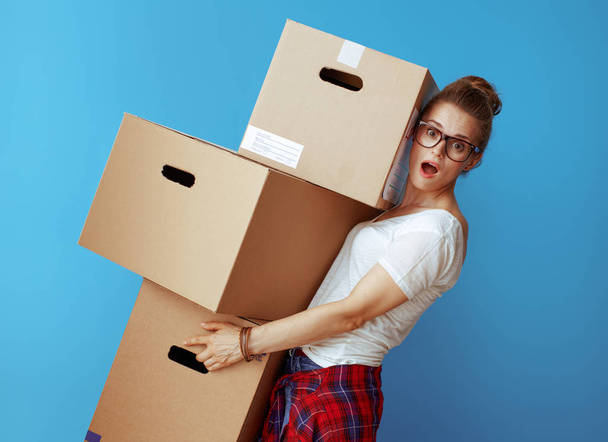 shocked modern woman in white t-shirt holding pile of cardboard boxes on blue background - Φωτογραφία, εικόνα
