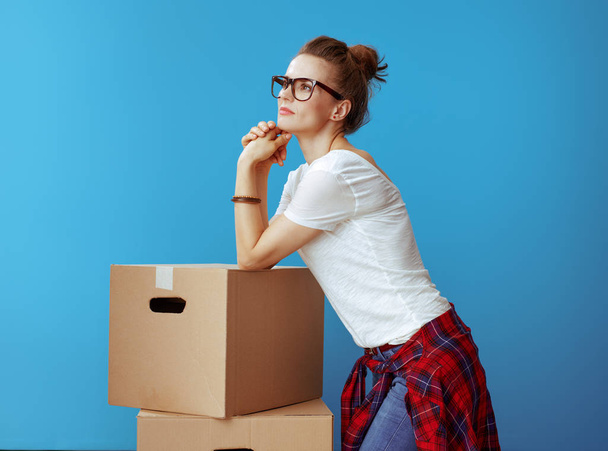 Portrait of pensive modern woman in white t-shirt near cardboard boxes isolated on blue background - Фото, зображення